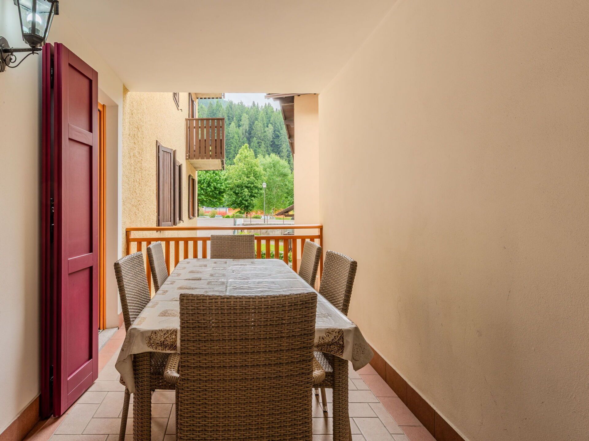 A balcony with a table and chairs, a view of trees, and a red door.