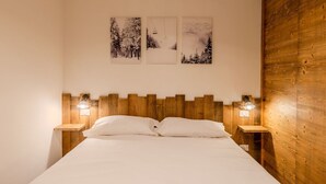 Ein Schlafzimmer mit einem Holzkopfteil, einem Bett mit weißer Bettwäsche und zwei Nachttischen mit Wandleuchten.