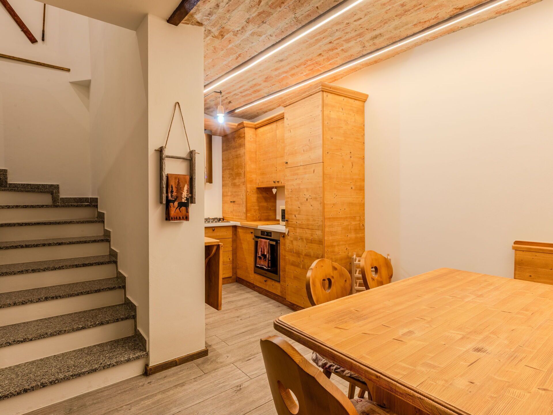 A wooden dining table with chairs, a kitchen area with wooden cabinets, and a staircase with granite steps.
