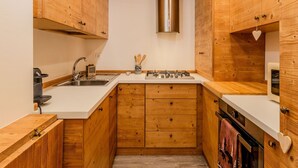 Eine kleine Küche mit Holzausstattung, einem Edelstahlspülbecken, einem Gasherd und einer Mikrowelle.