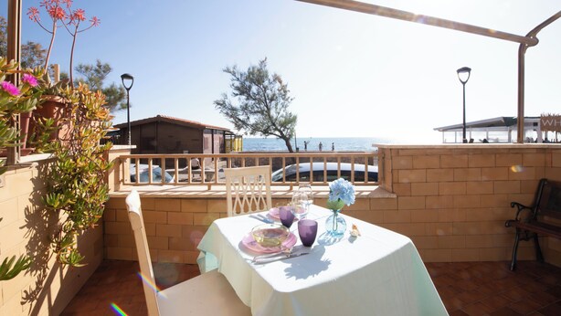 A terrace with a table set for dining, overlooking a body of water and a building in the background. - Jade house facing the sea just a stone's throw from Rome (Ladispoli)