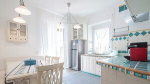 A kitchen with white cabinets, a refrigerator, a sink, and a dining area with a table and chairs. - Jade house facing the sea just a stone's throw from Rome (Ladispoli)