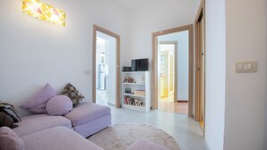 A modern living room with a sofa, a television on a shelf, and a bookshelf. - Jade house facing the sea just a stone's throw from Rome (Ladispoli)