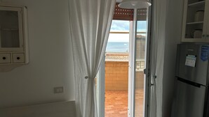 A kitchen with a refrigerator, a window with curtains, and a view of the beach. - Jade house facing the sea just a stone's throw from Rome (Ladispoli)