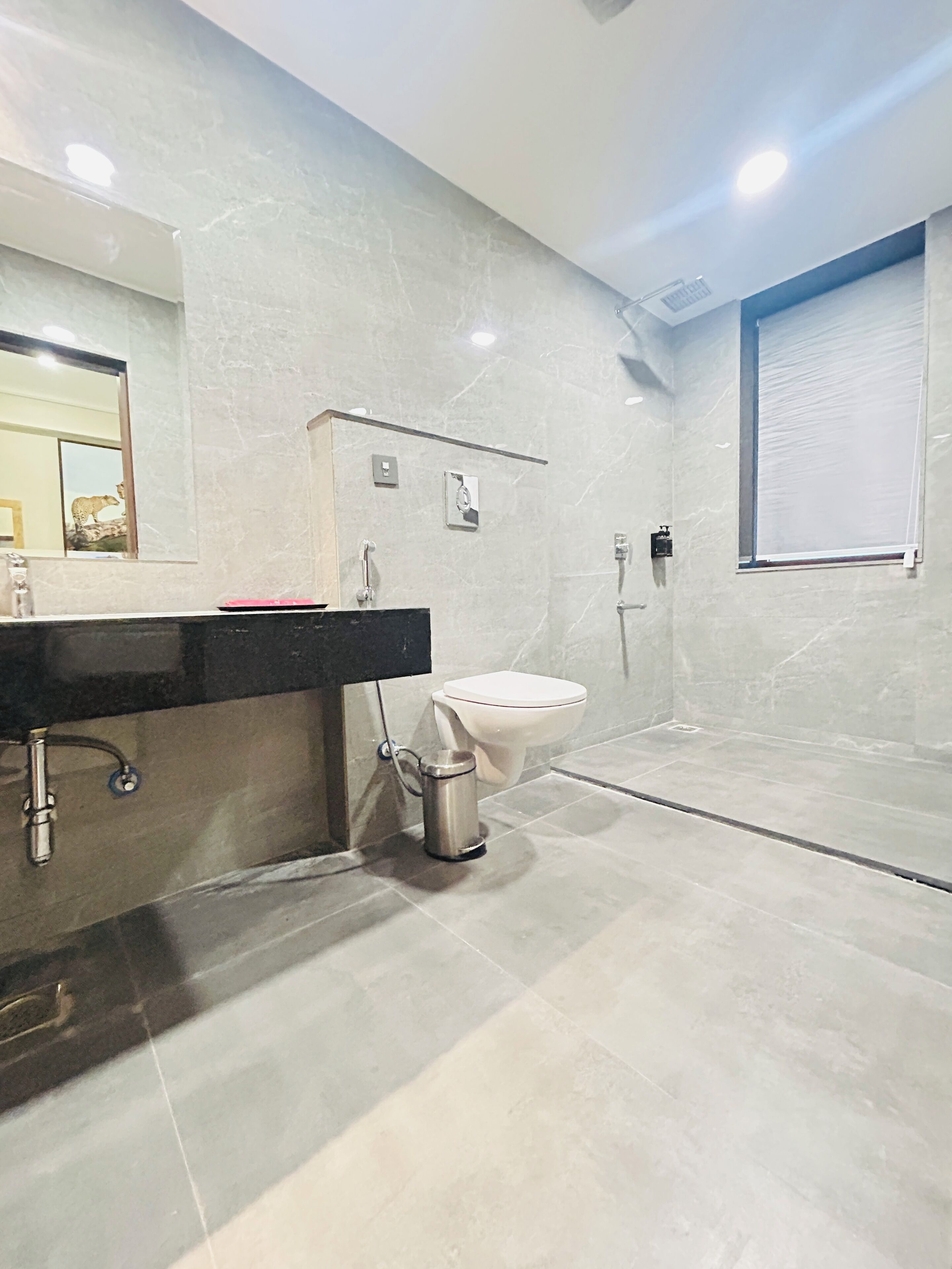 A modern bathroom with a marble floor, a black sink, a white toilet, and a shower area.