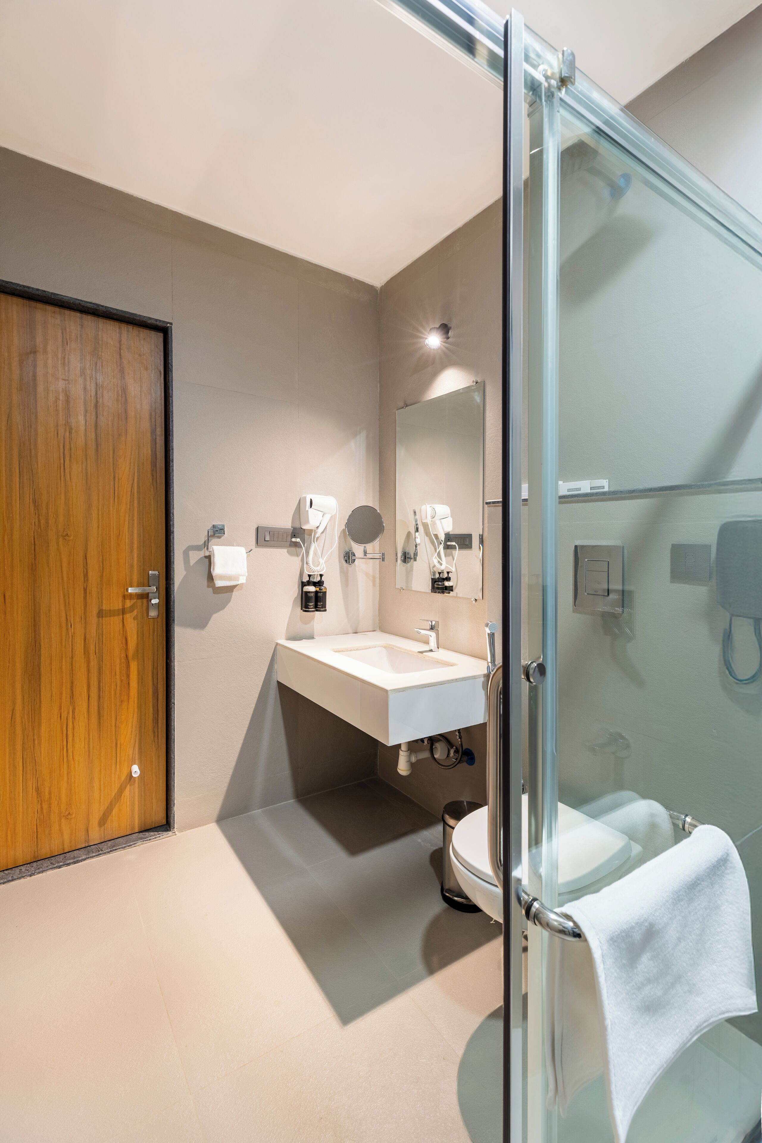 Un bagno moderno con box doccia in vetro, porta in legno, lavabo bianco e water.