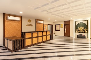 A hotel reception area with a check-in counter, air conditioning units, and a decorative wall with a logo. - The Fort Resort by Namoka (Kumbhalgarh)