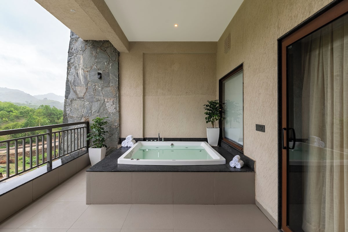 A balcony with a hot tub, a potted plant, and a view of greenery and mountains.