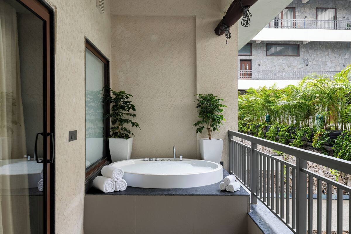 A bathroom with a large bathtub, two potted plants, and a balcony with a railing.