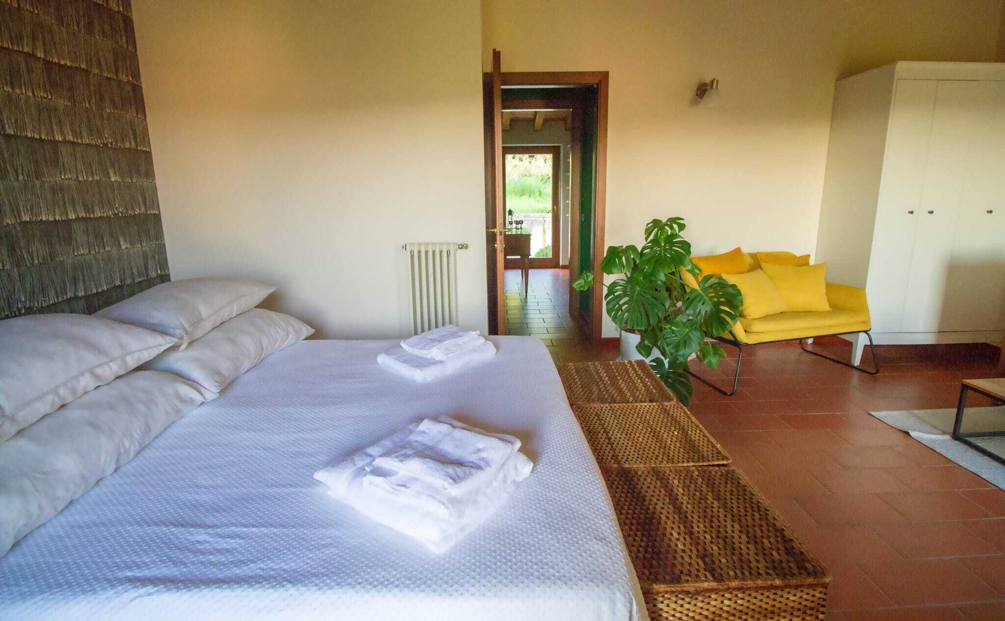Camera da letto con un letto grande, una testiera in legno, un termosifone, una sedia gialla, una pianta e un armadio.