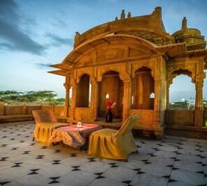 Un espace extérieur aménagé de manière traditionnelle, avec une architecture richement décorée, une table agrémentée d’un vase et une vue sur le paysage.