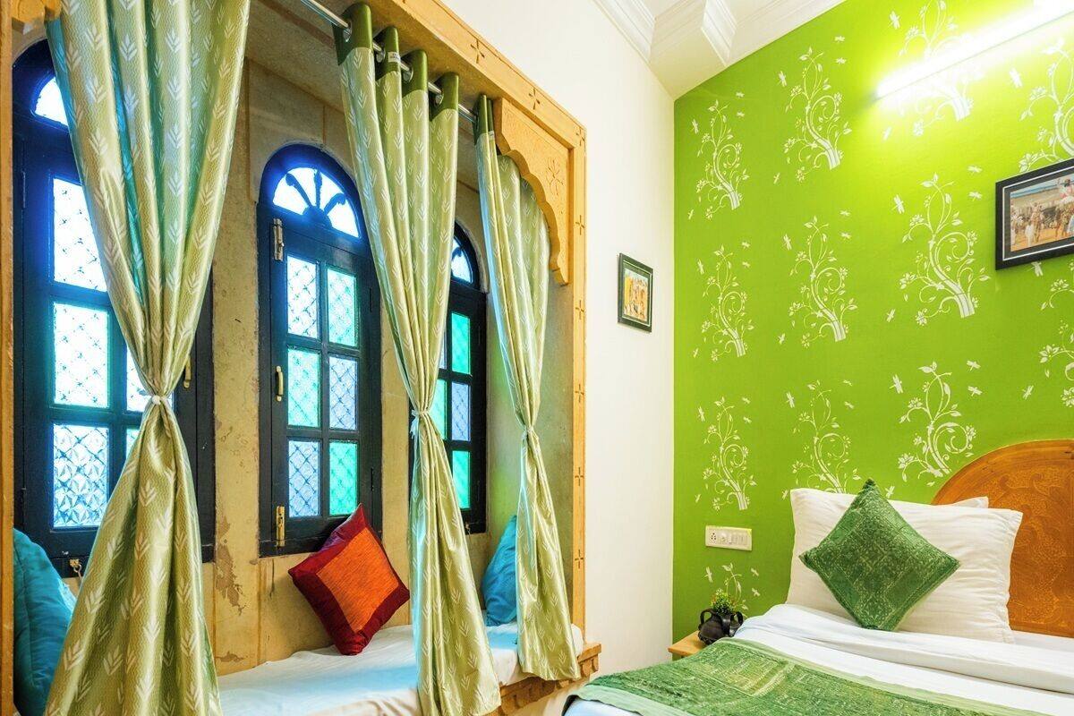 Une chambre avec un lit, une fenêtre avec des rideaux, un mur vert orné de motifs floraux et une tête de lit en bois.