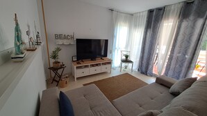 Ett vardagsrum med en soffa, en tv, ett litet bord med en växt och en skylt med texten ”STRAND”.