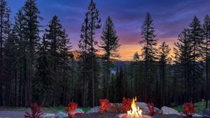 A fire pit surrounded by rocks and red foliage in a forested area. - Luxury Home | Ski In / Ski Out | 5 Bed / 4 Bath (Whitefish)