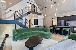 Interior moderno com um sofá verde, uma mesa de centro preta, uma escada e uma área de cozinha.