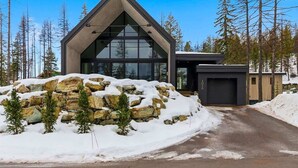 A modern building with a triangular roof, large windows, and a garage. - Luxury Home | Ski In / Ski Out | 5 Bed / 4 Bath (Whitefish)