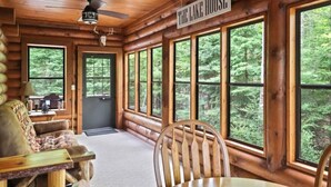 L’intérieur d’une cabane avec une grande fenêtre, un ventilateur de plafond, une enseigne indiquant « The Lake House » et un banc en bois près de la porte.