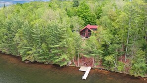 Une cabane entourée d’une forêt dense, avec une jetée qui s’avance sur une étendue d’eau.