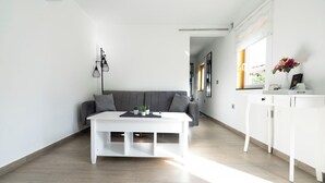Un salón moderno con un sofá gris, una mesa de centro blanca y un armario blanco con un florero.