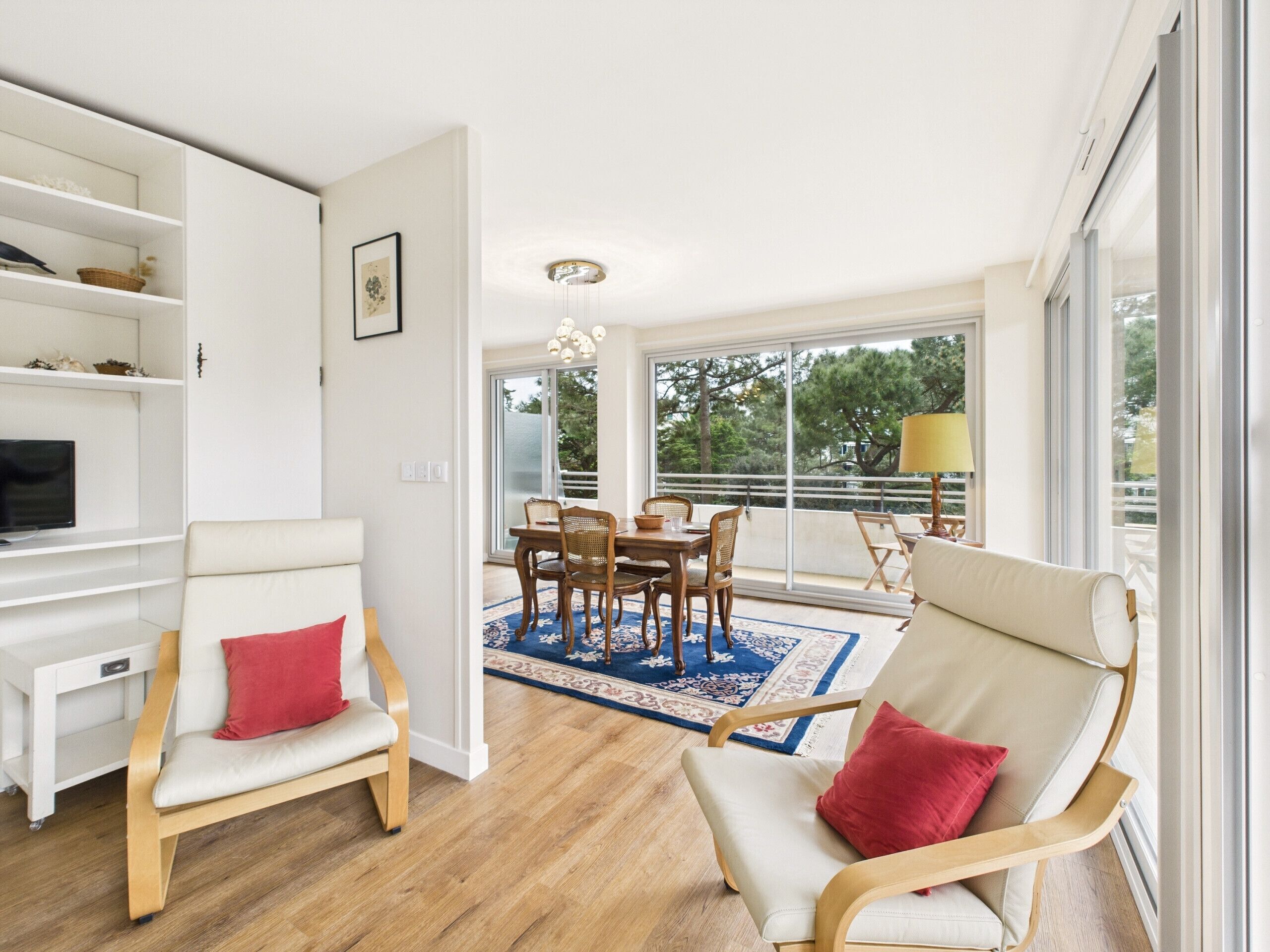 Un salon moderne avec un coin repas, de grandes fenêtres et une vue sur les arbres.