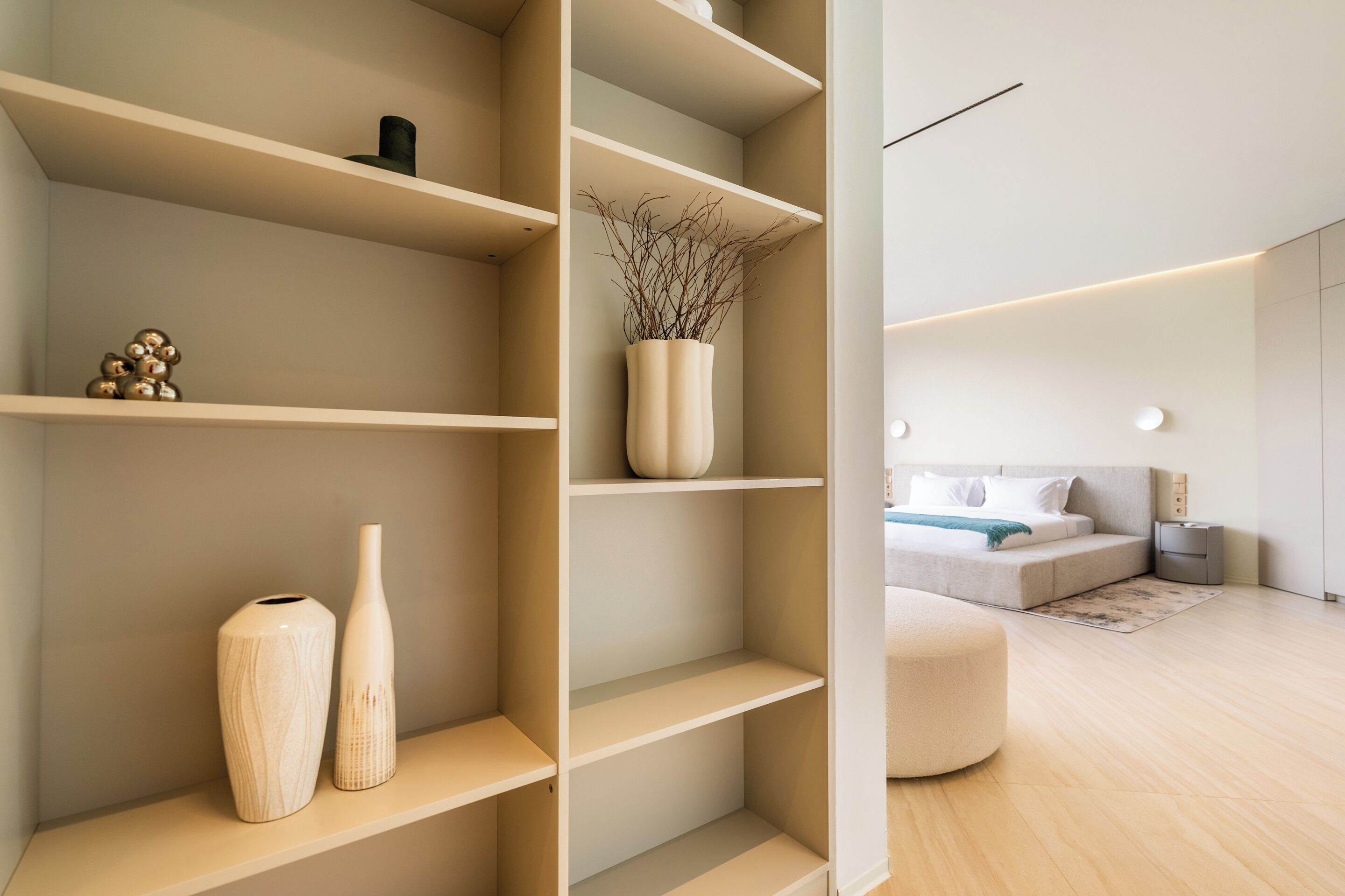 A modern interior with a minimalist design, featuring a large shelving unit with decorative items, a bed with a neutral color scheme, and a clean, uncluttered space.