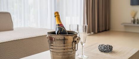 Eine Minibar mit einer Champagnerflasche, einem Glas und einer Fernbedienung auf einem Holztisch im Hotelzimmer.