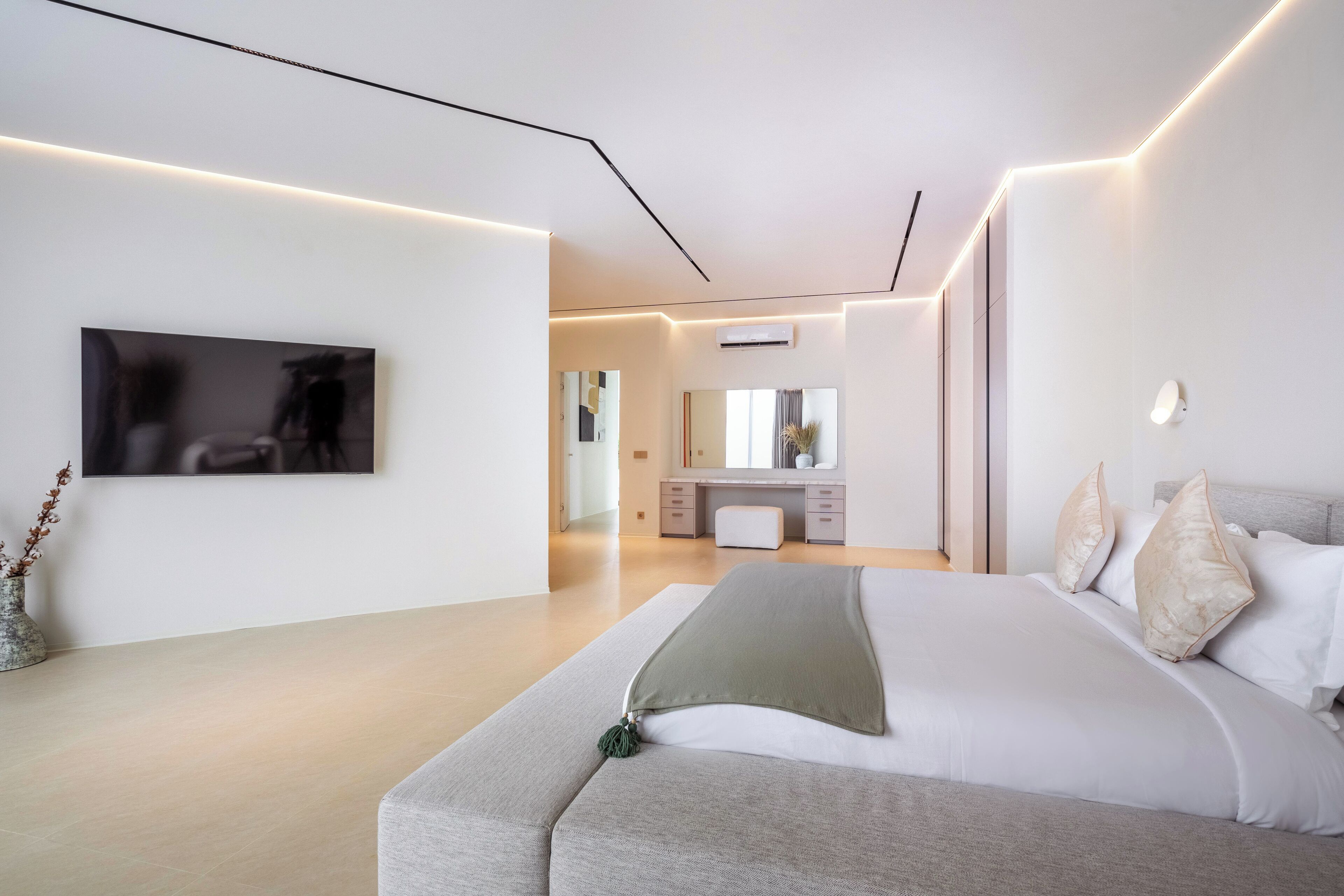 A modern bedroom with a large bed, a flat-screen TV mounted on the wall, and a minimalist design.