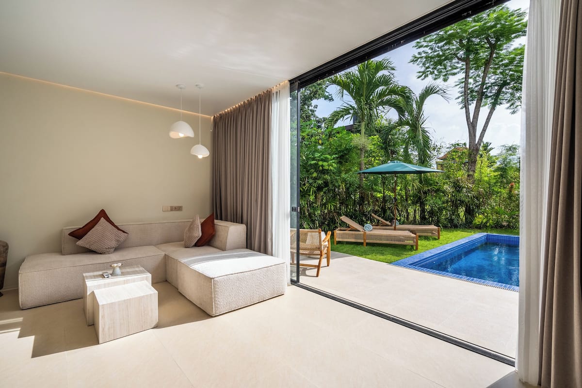 A modern living room with a large glass door leading to a pool area, a sofa with cushions, and a small coffee table.