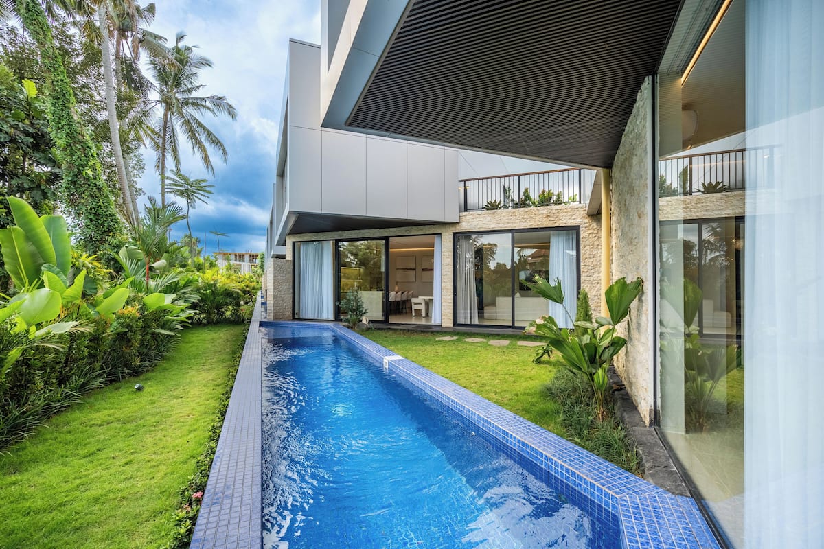 A modern house with a swimming pool, a covered patio, and lush greenery.