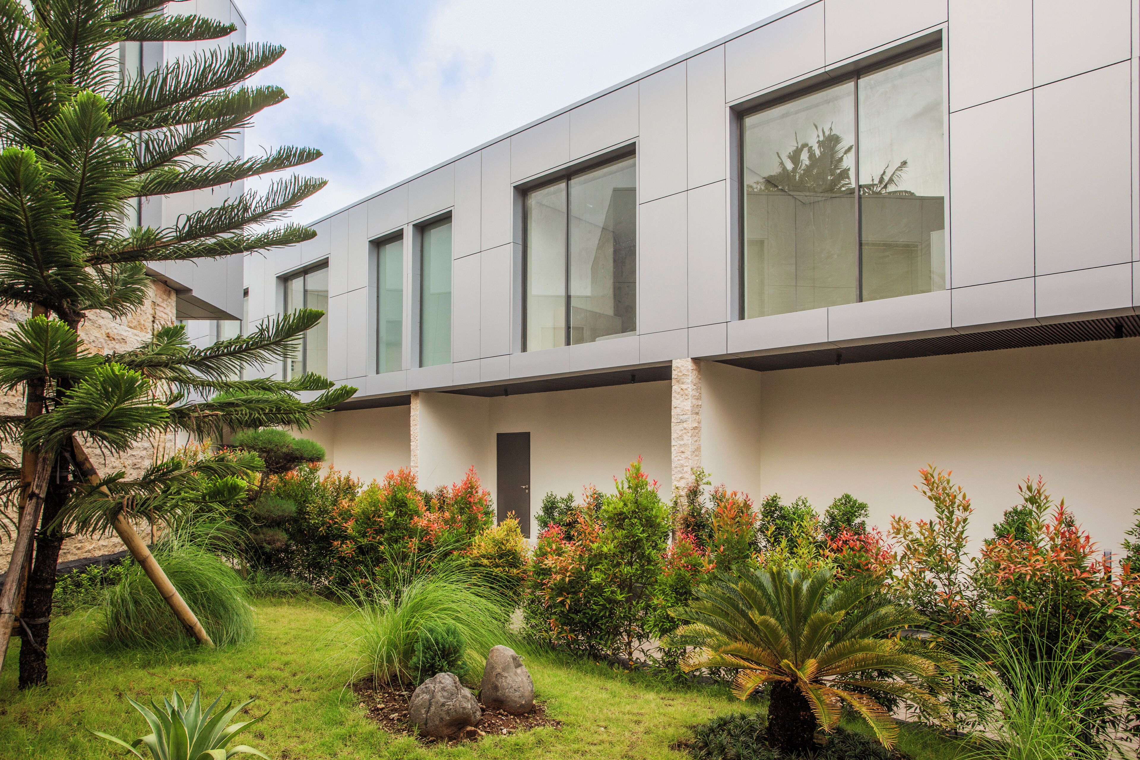 A modern building with large windows and a well-maintained garden with various plants and rocks.