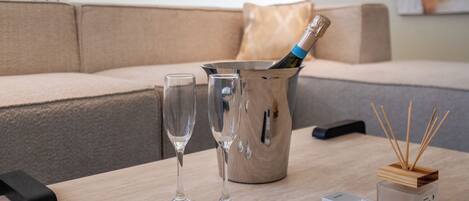 Ein modernes Wohnzimmer mit einem beigen Sofa, einem Holztisch, zwei Sektgläsern, einer Champagnerflasche, einer Fernbedienung und einem Reed-Diffusor.