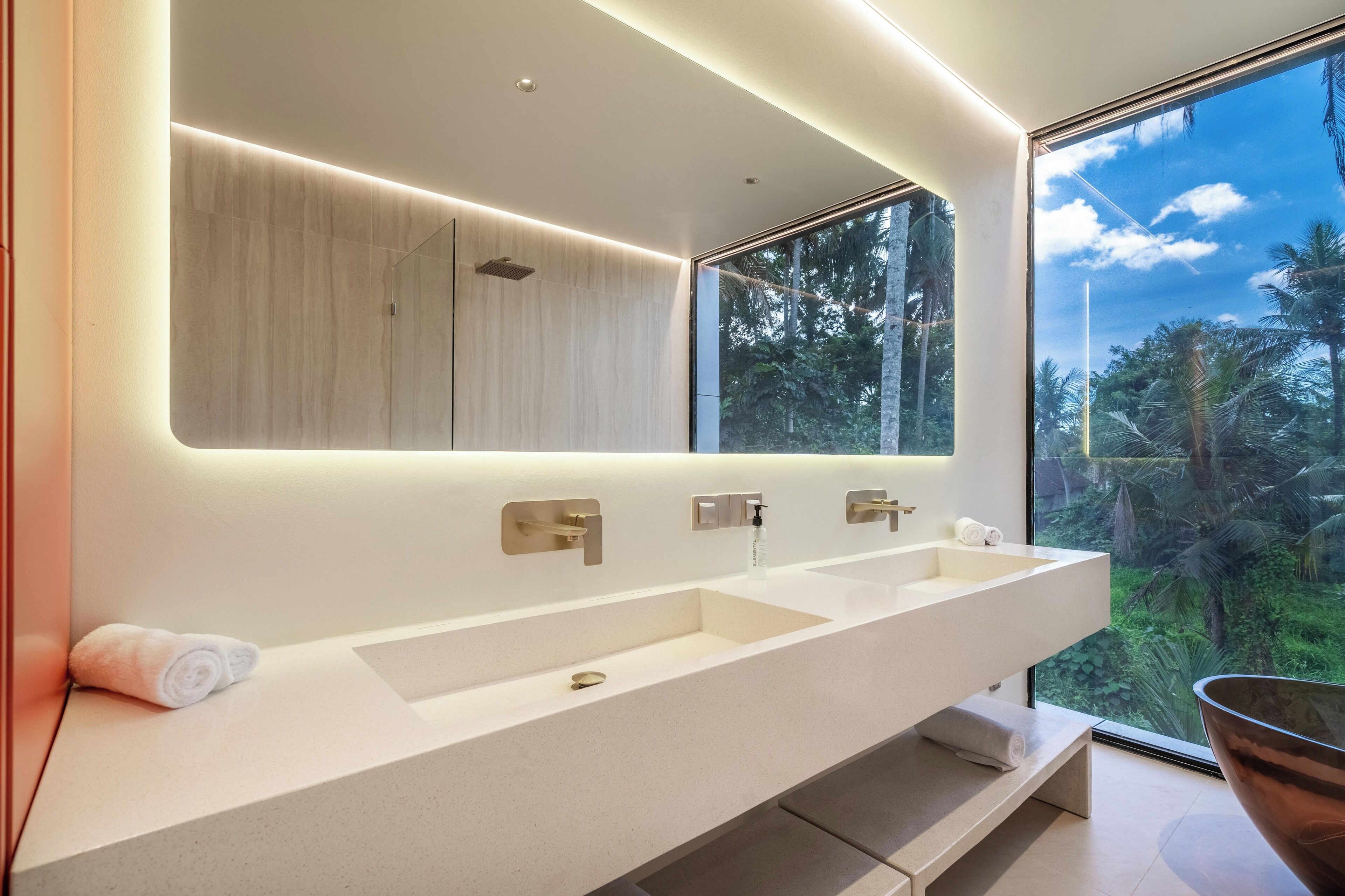 Un bagno moderno con uno specchio grande, due lavandini e vista su un paesaggio tropicale.