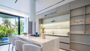Una cocina moderna con una isla central, taburetes de bar y vista a una piscina.