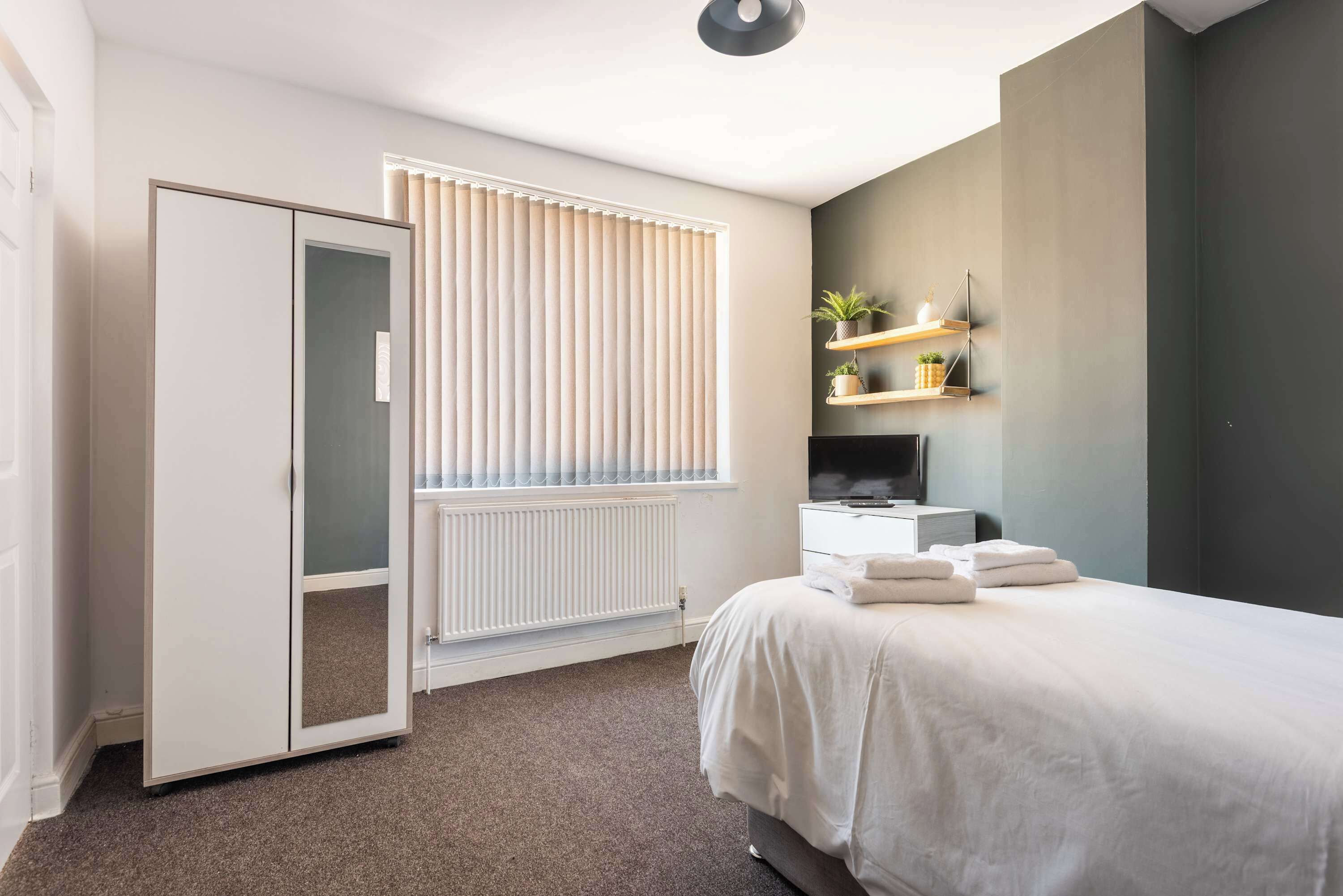 Un dormitorio moderno con una cama, un armario, un radiador y una estantería con plantas.