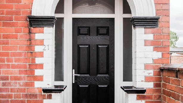 A red brick building with a black door, white trim, and a small porch.