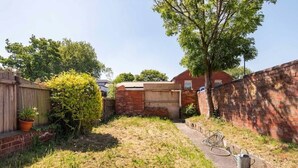 A backyard with a brick wall, a wooden fence, a tree, and a hose. - Convenient Budget Room in Shared House w Kitchen (Doncaster)