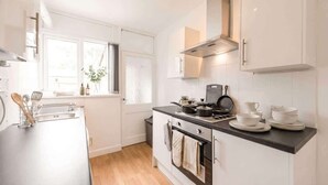 A modern kitchen with white cabinetry, a black countertop, and a window with blinds. - Convenient Budget Room in Shared House w Kitchen (Doncaster)