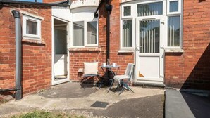 A red brick building with a white door, a satellite dish, and a small outdoor seating area with two chairs and a table. - Convenient Budget Room in Shared House w Kitchen (Doncaster)