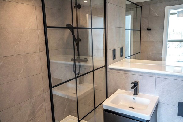 A modern bathroom with a glass-enclosed shower, a white sink, and a large mirror.