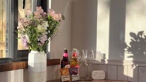A wooden bar area with a vase of flowers, two bottles of Sandford chocolate cookies, and wine glasses. - Whimple Shepherd Hut, Sleeps 2, Wood Fire & Garden (Exeter)