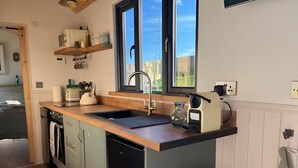A compact kitchen with a wooden countertop, a built-in sink, and a small trash bin. - Whimple Shepherd Hut, Sleeps 2, Wood Fire & Garden (Exeter)