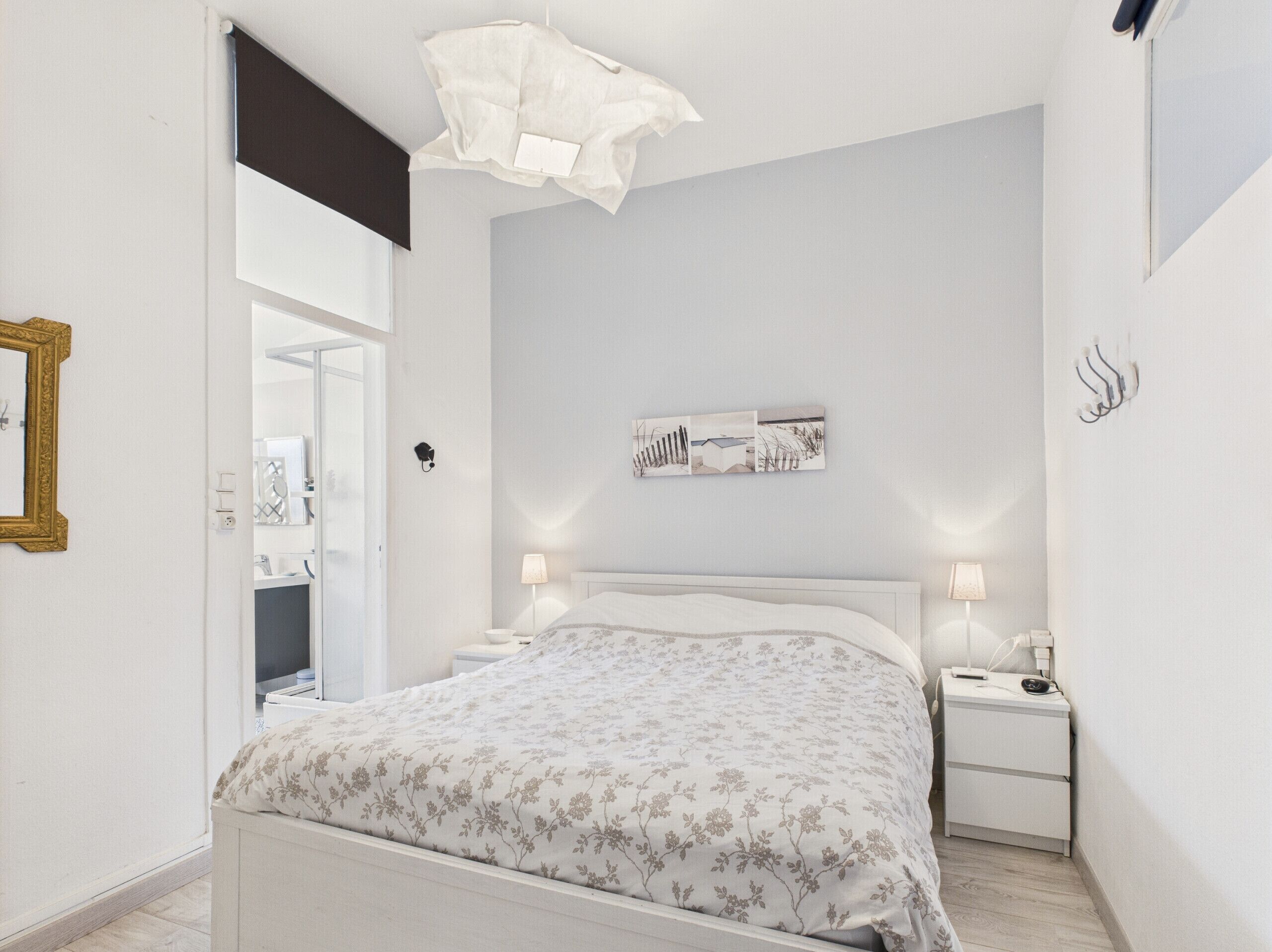 Een slaapkamer met een bed, nachtkastjes, een wandlamp, een ingelijst schilderij en een deur naar een andere kamer.