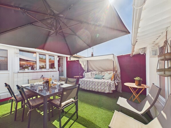A patio with a table and chairs, a covered seating area, and a view of the street.