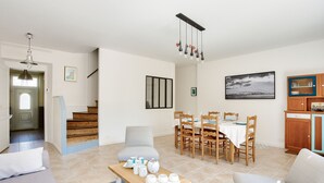 A spacious living room with a sofa, a coffee table, and a dining area with a table and chairs. A staircase is visible in the background.