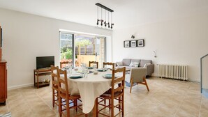 A dining area with a table set for four, a television on a stand, and a sofa in the background.