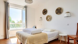 A bedroom with a bed, a wooden floor, a window with curtains, and wall-mounted lamps.