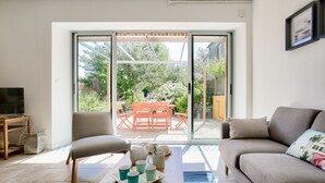 A living room with a sofa, a coffee table with cups, a TV, and a sliding glass door leading to an outdoor patio with a table and chairs.