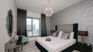 A modern bedroom with a large bed, a bedside table, a mirror, and a view of the city. - Bellavista - Spacious -1BR & Extra Room  (Dubai)