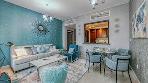 A modern living room with a sofa, coffee table, and chairs, a dining area with a table and chairs, and a kitchen visible through an open doorway. - Bellavista - Spacious -1BR & Extra Room  (Dubai)