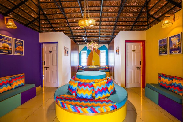 A vibrant, circular seating area with colorful zigzag cushions, a ceiling with a corrugated metal design, and a central chandelier. - goSTOPS Coorg (Madikeri)